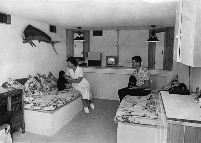 Mrs. Stewart and her son, David, relax in their multiple-use fallout shelter. The interior of the shelter mimics the comforts of home, with two beloved dogs, a TV, telephone and wall décor. August 3, 1964. Charles Trainor photographer. Miami News Collection, HistoryMiami. 1989-011-3875.