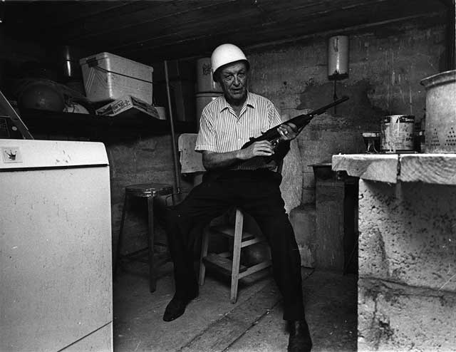 Dr. F. Archer poses with his rifle at ready in a sparsely furnished cinderblock shelter. March 7, 1967. Jay Spencer photographer. Miami News Collection, HistoryMiami. 1989-011-3882.