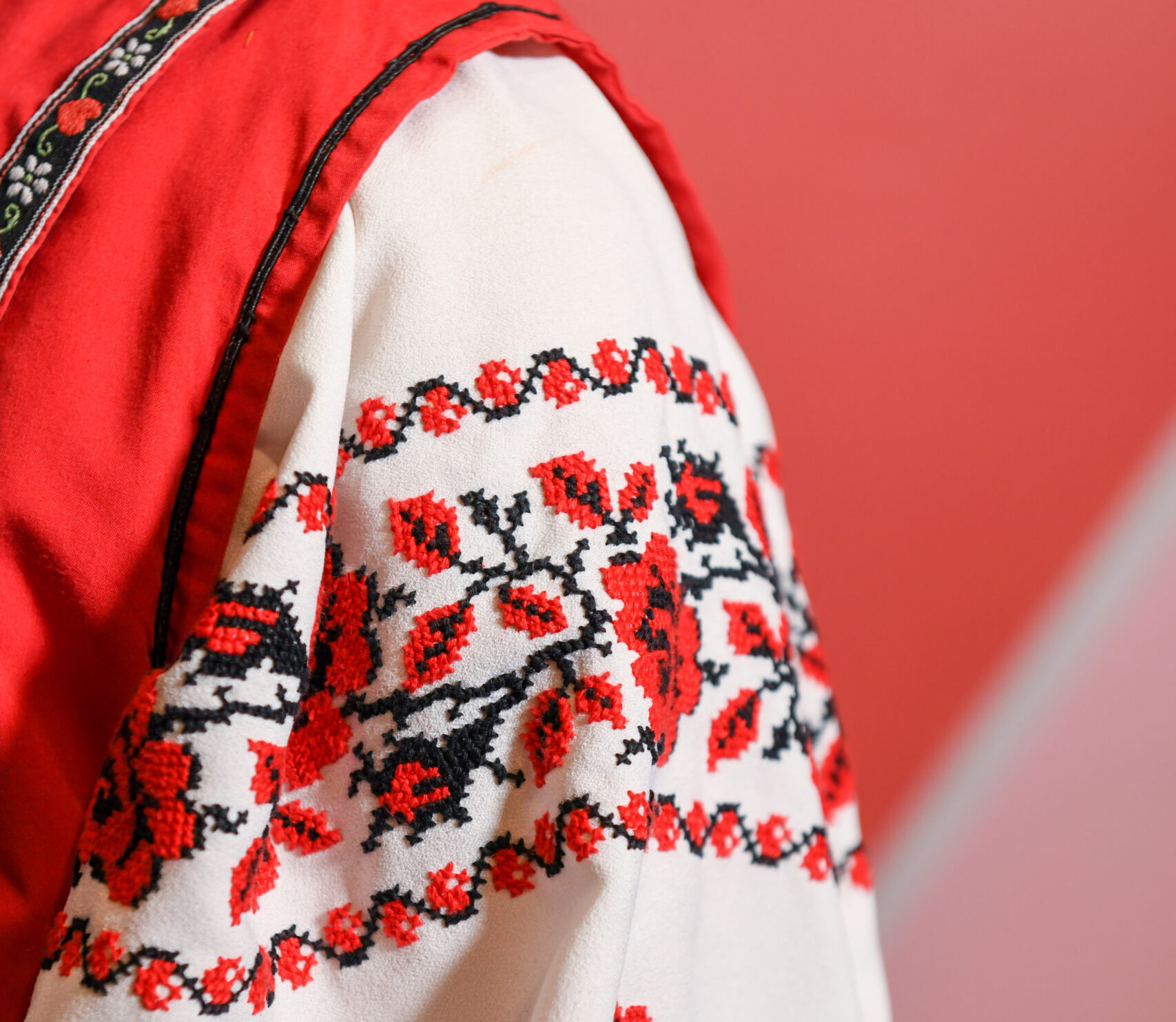 Red and black embroidery detail on the shoulder of a dancer's white shirt.