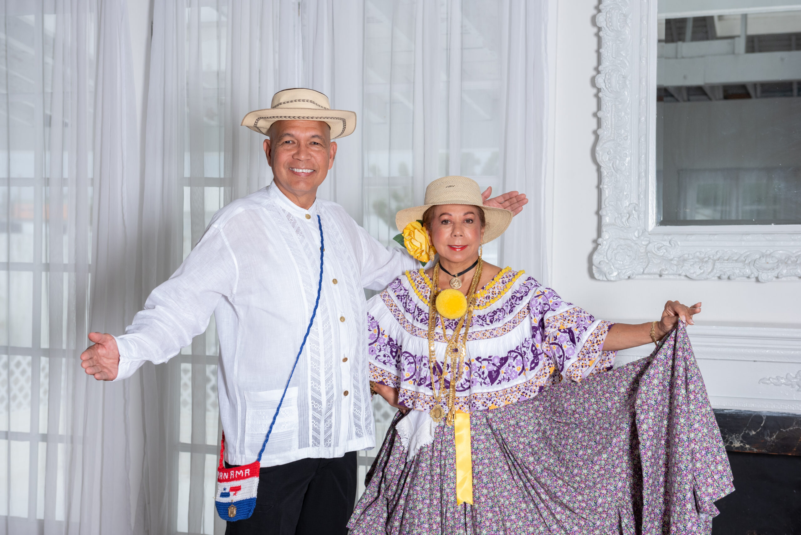 A man in a white shirt and straw hat poses with a woman in a purple and white embroidered dress and a straw hat.