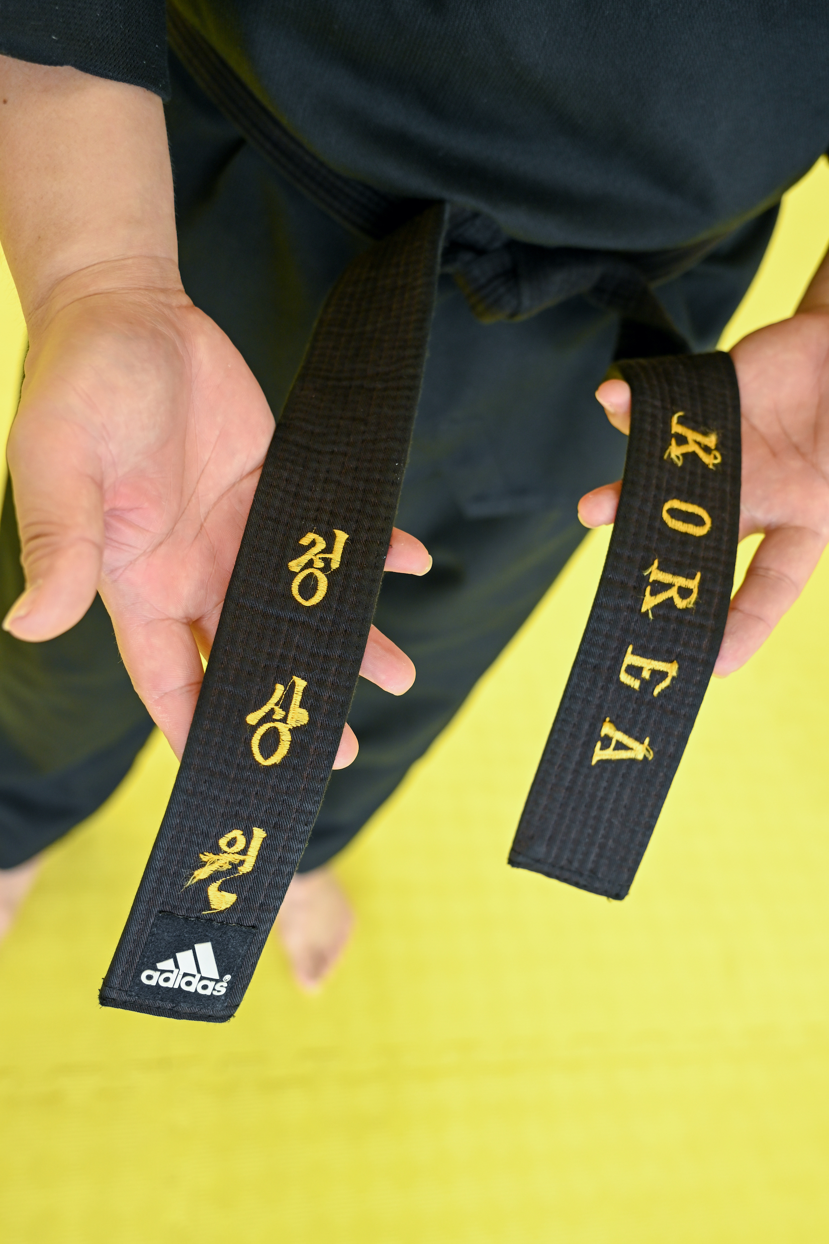 Master Jeong holds up the ends of his black belt. One side has the word 