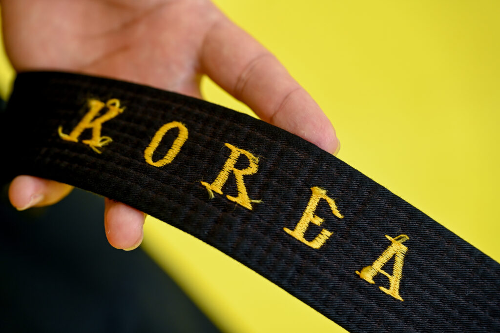 Close up shot of black belt with "Korea" embroidered in black.