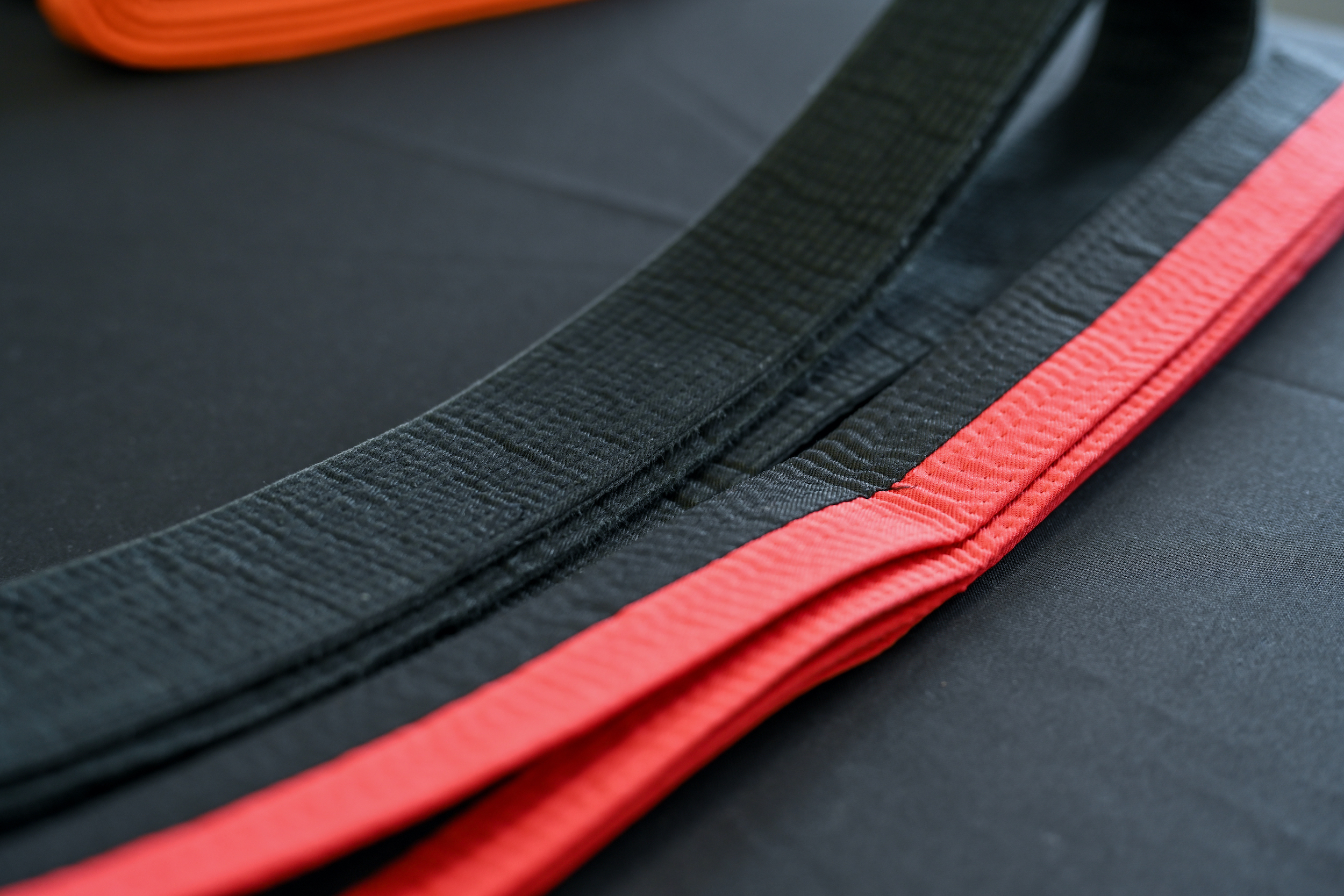 A black belt and a belt that is half red and black sit on a table.