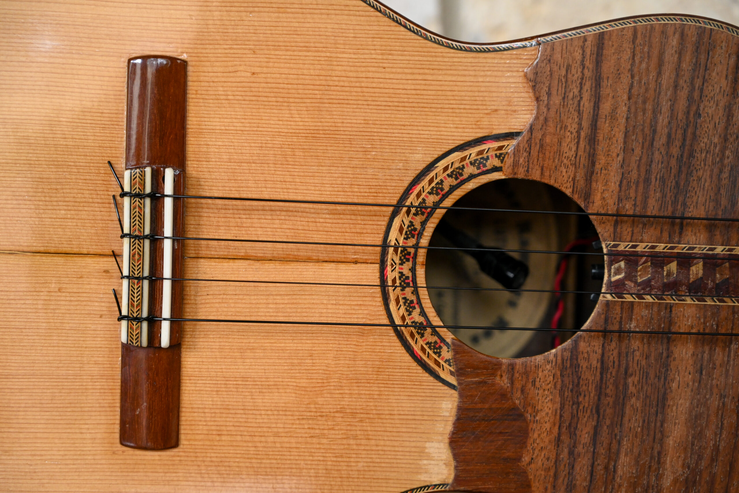 A close up of the strings and sound hole of the cuatro guitar. The guitar has four strings.