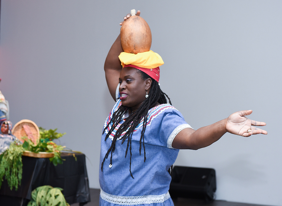 Ketsia Theodore Pharel holds a gourd on her head and outstretches her arm.