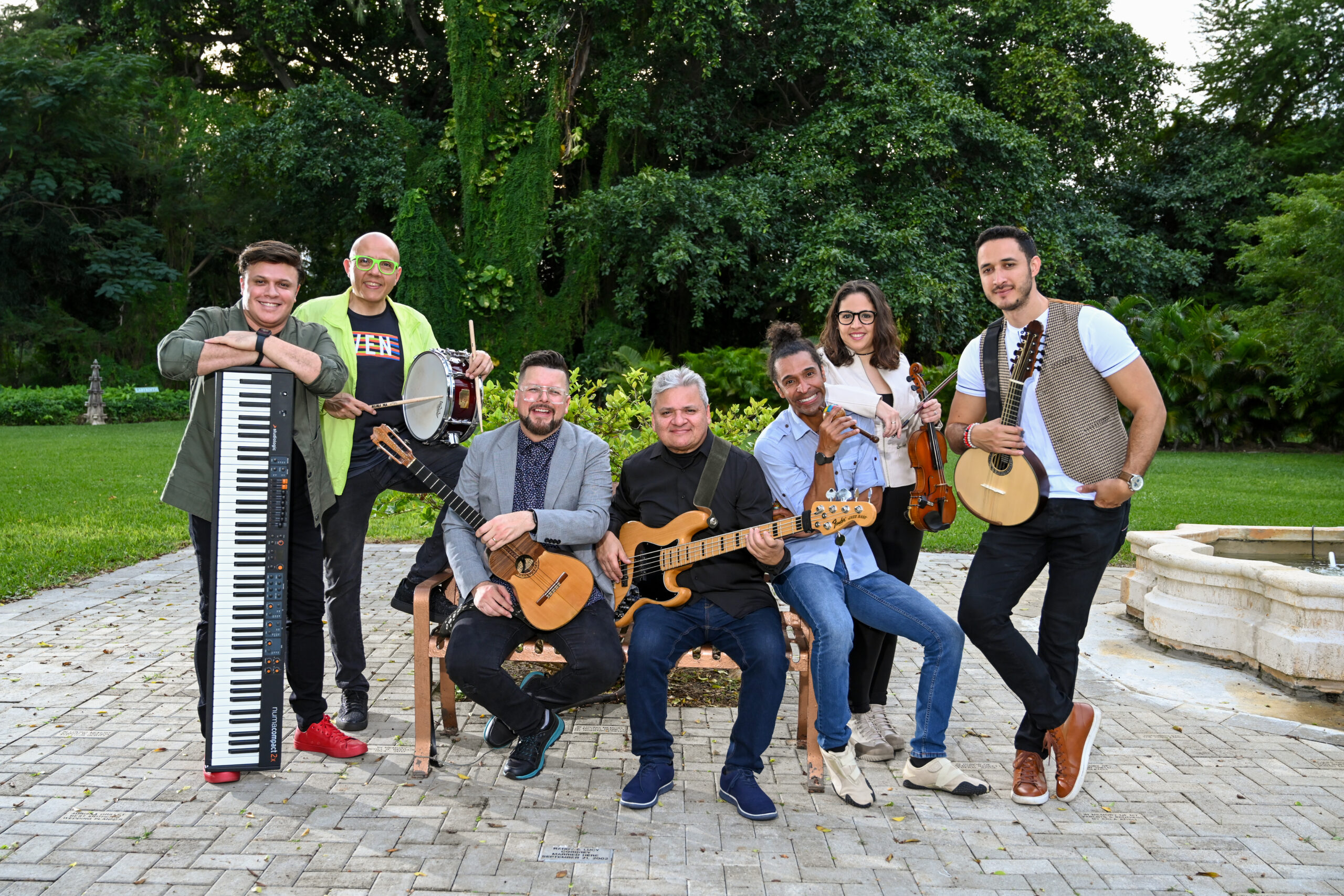 The Henry Linarez Ensemble includes seven musicians seated and standing around a bench, each holding their instrument: keyboard, snare drum, cuatro, bass, maracas, violin, and mandolin