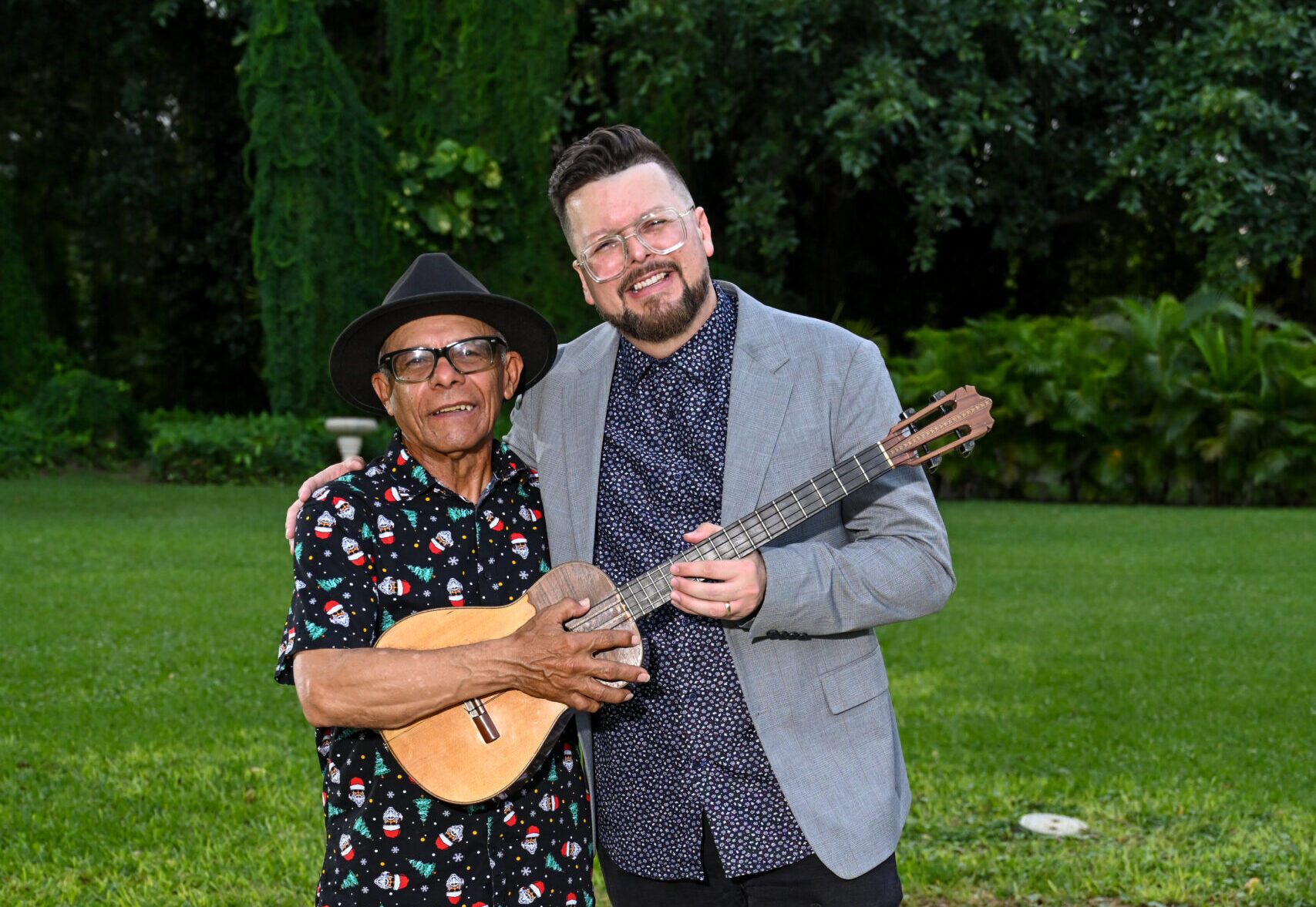 Henry Linarez poses with his father as they both hold the cuatro guitar in their hands.