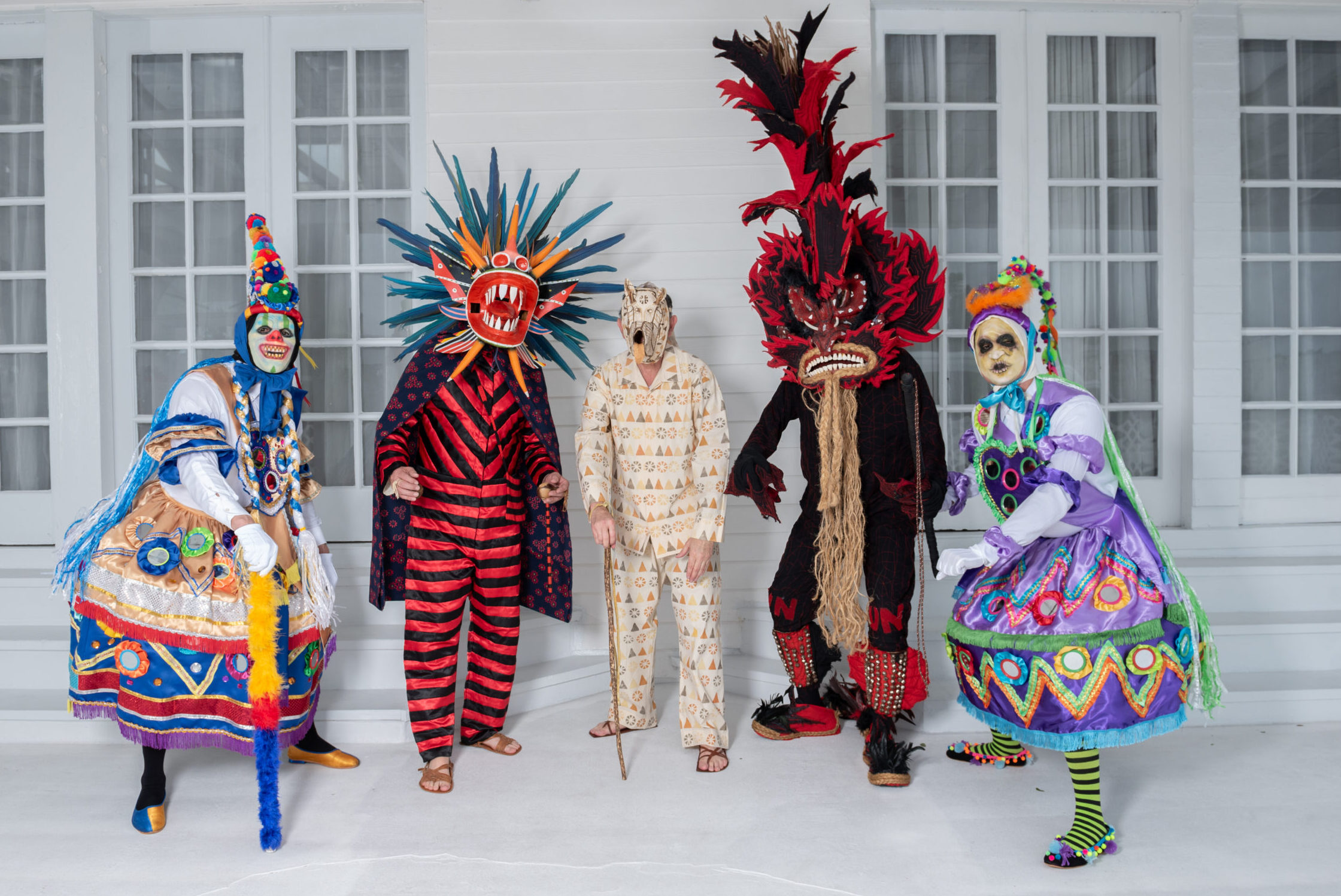 Five people in different costumes pose for a photo. Each costume is different and includes elaborate headpieces, masks, and outfits.