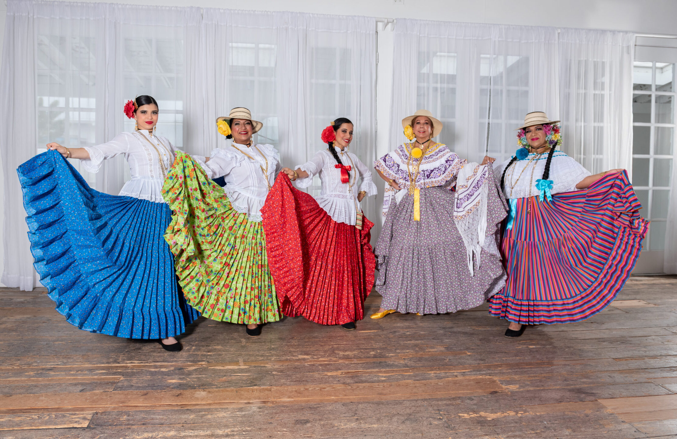 Five women wearing long colorful skirts and different kinds of embroidered and lace tops pose for a photo with their skirts fanned out.