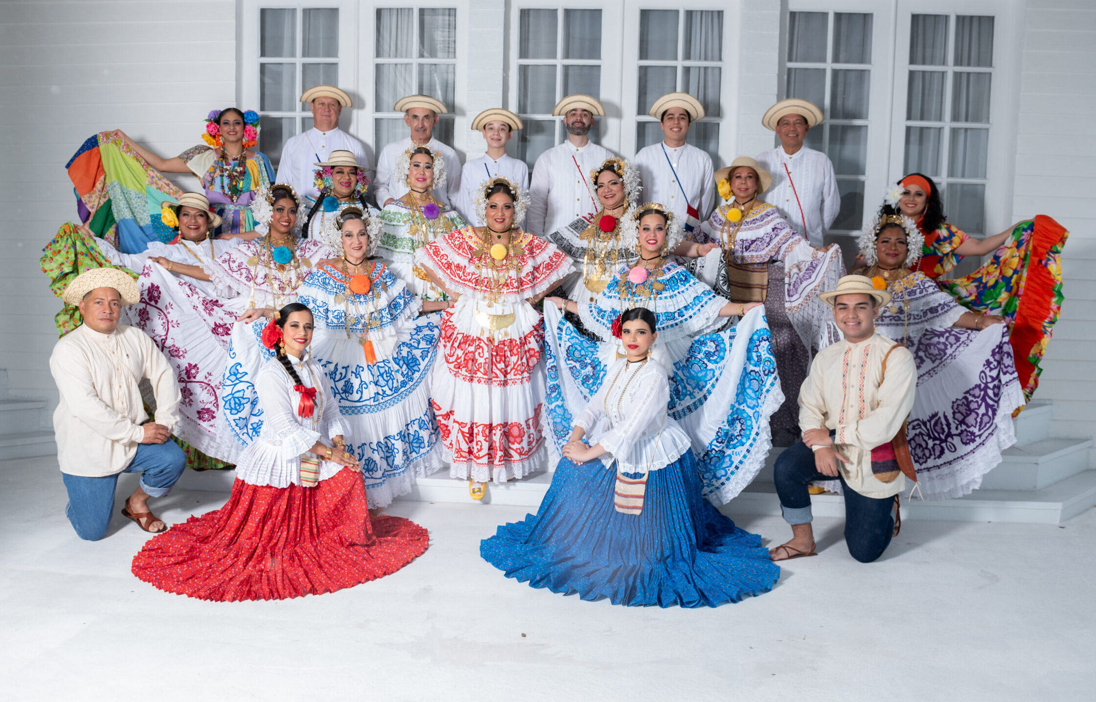 The full dance ensemble poses for a photo in various traditional costumes. There are 22 members and the group is comprised of both men and women.