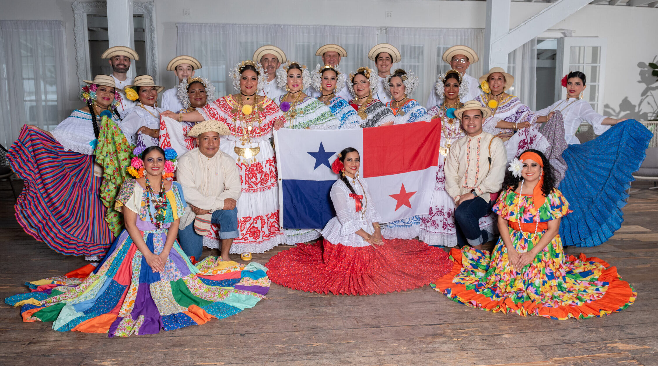 The full dance ensemble poses for a photo in a variety of costumes. Members in the front row hold up the Panamanian flag.