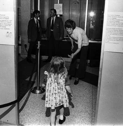 Airport employee Mary Wein beckons a little girl through a metal detector in the Eastern Airlines terminal at Miami International Airport. August 11, 1973. Miami News Collection, HistoryMiami. 1989-011-9987.