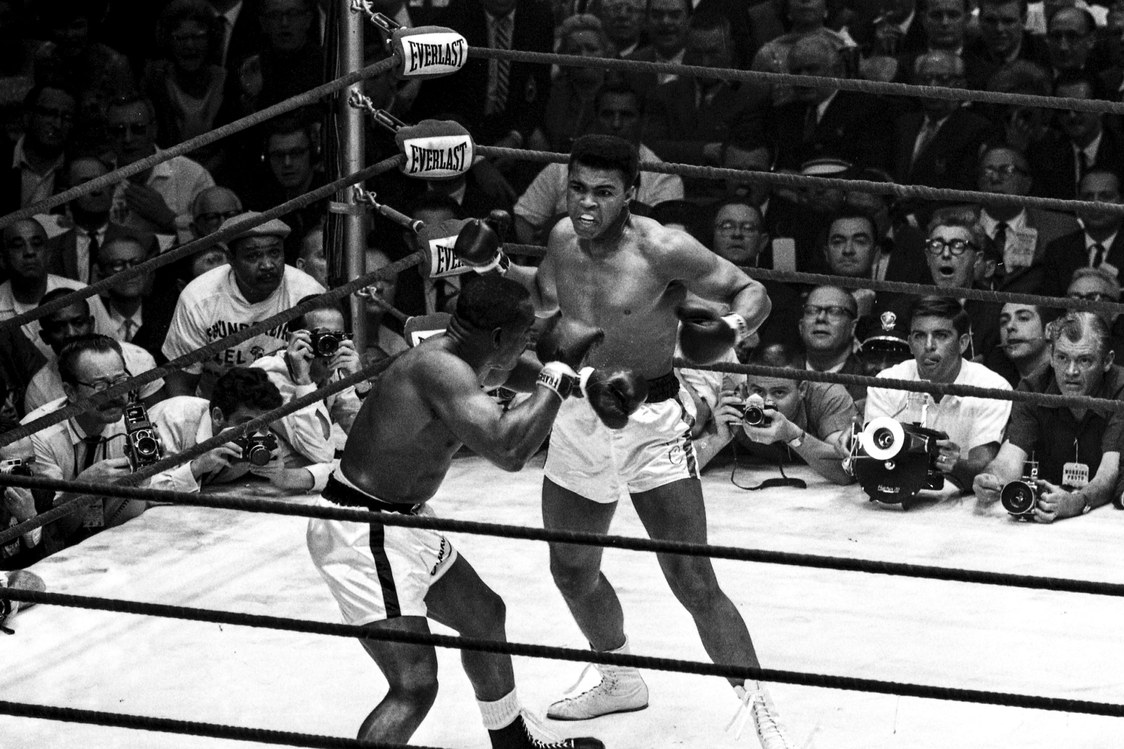 Muhammad Ali in the ring with opponent Sonny Liston. In the background are spectators in the audience.