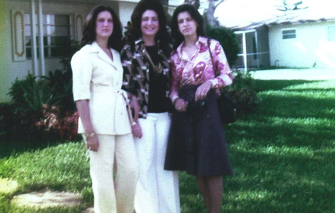 Three women, Ana M. Gallego, her mother, and older sister stand in a home's front lawn in 1975.