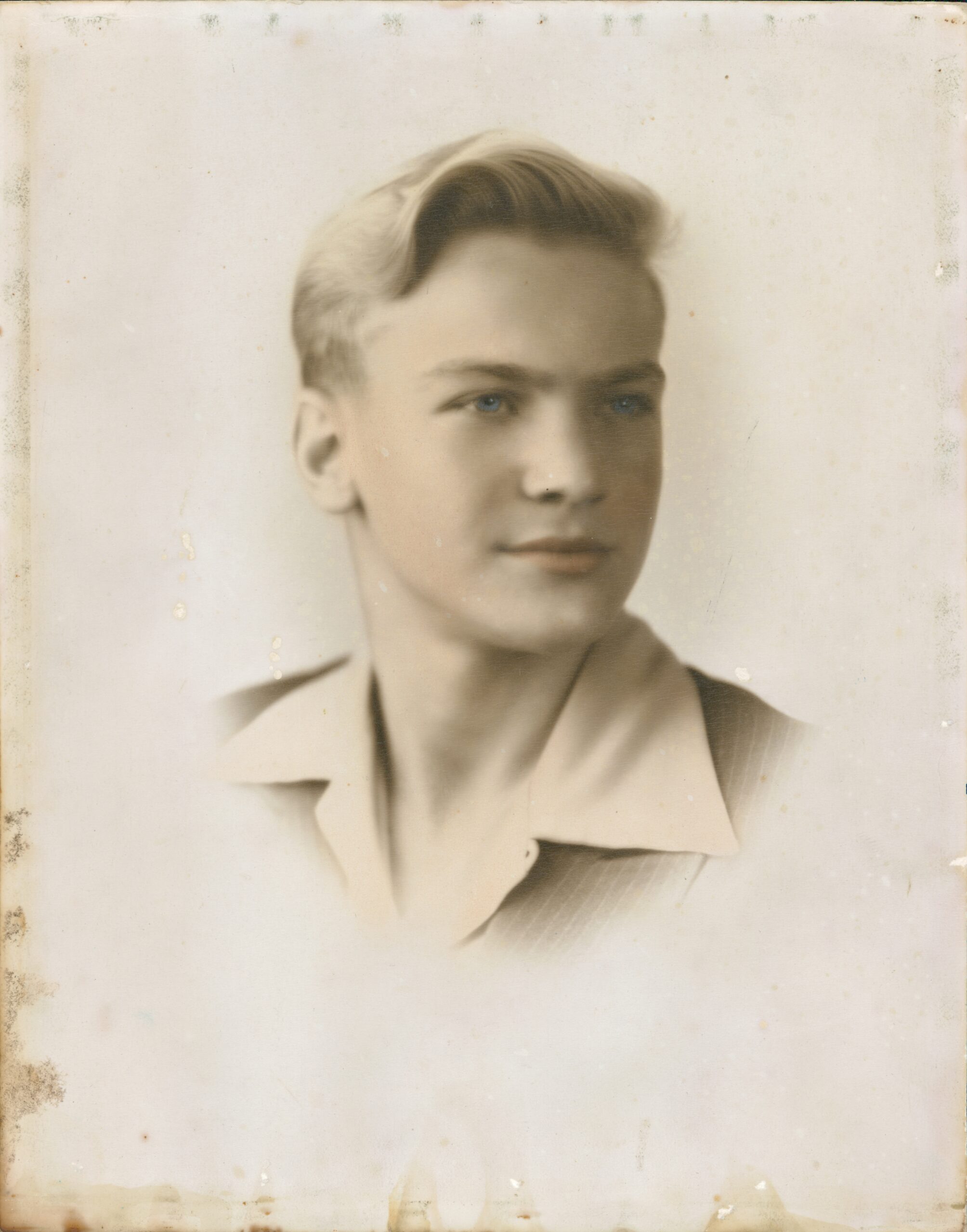 A black and white headshot of a young man with blonde hair and blue eyes.