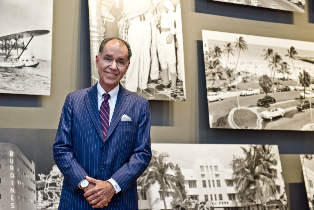 Dr. George stands in a blue suit with red tie before a black and white photography exhibition against grey walls.