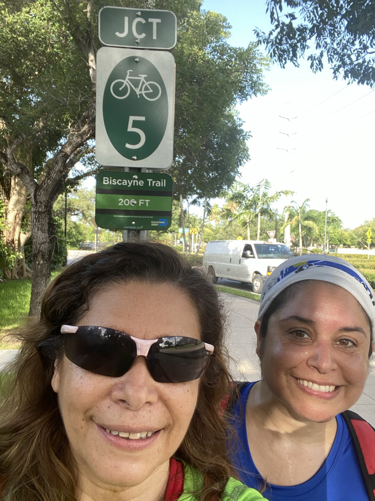 Two women smile in front of a sign that reads "Biscayne Trail"
