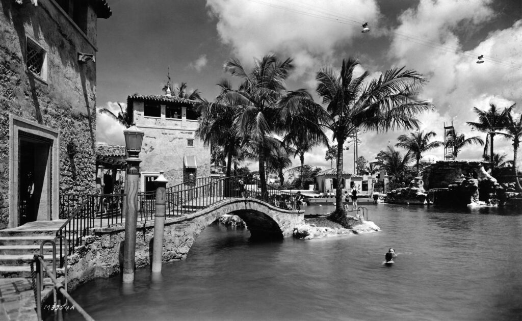 A black and white image of a Mediterranean styled outdoor pool with stone steps and arches leading out of it.