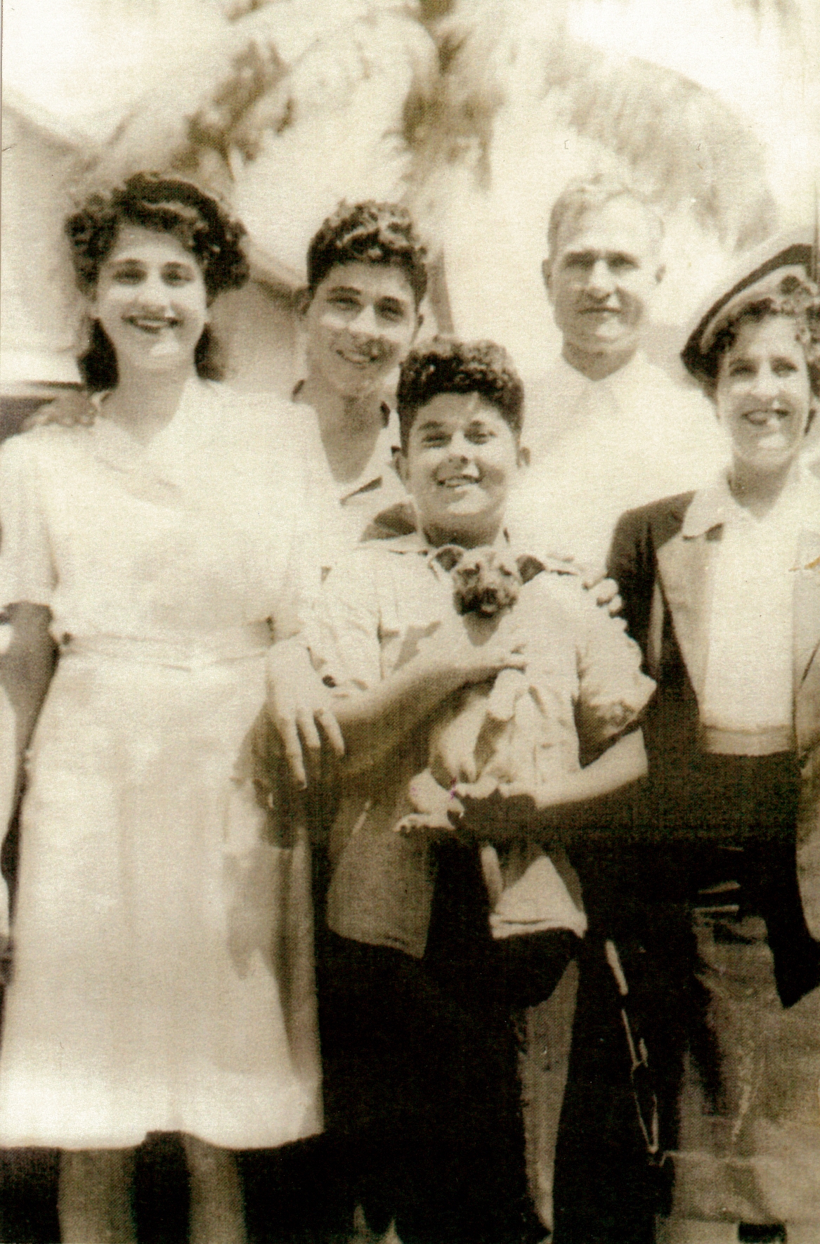 A black and white photo of the Nola family in 1939. The photo includes parents, Mike and Chafica, their teenage children Josephine and William, and youngest son Frank. Frank is holding a puppy.