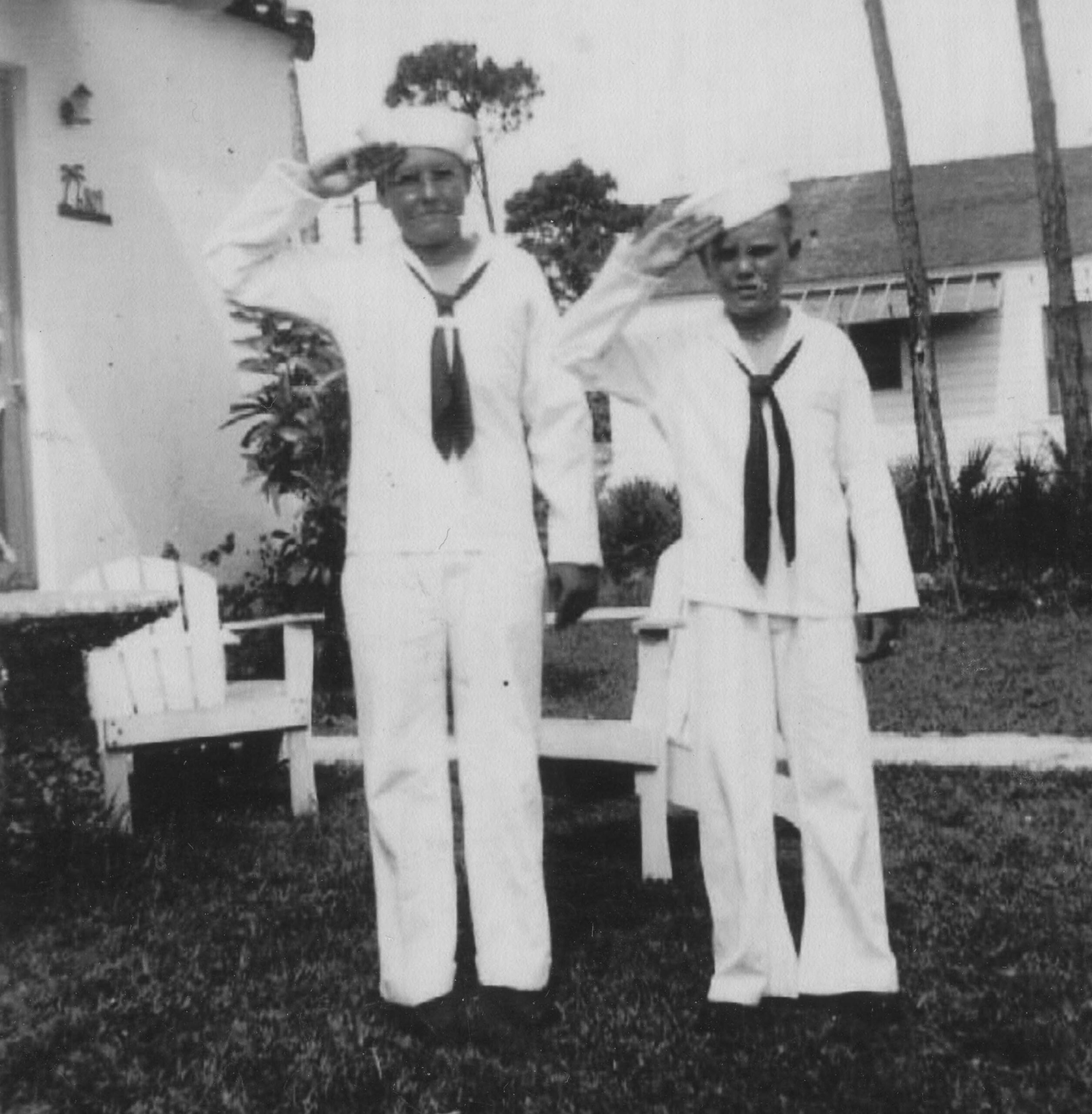 A black and white photo of Al Borden (Left) and Jerry Capley (right) dressed in Navy uniforms in 1942. The two are standing in a yard in a salute.