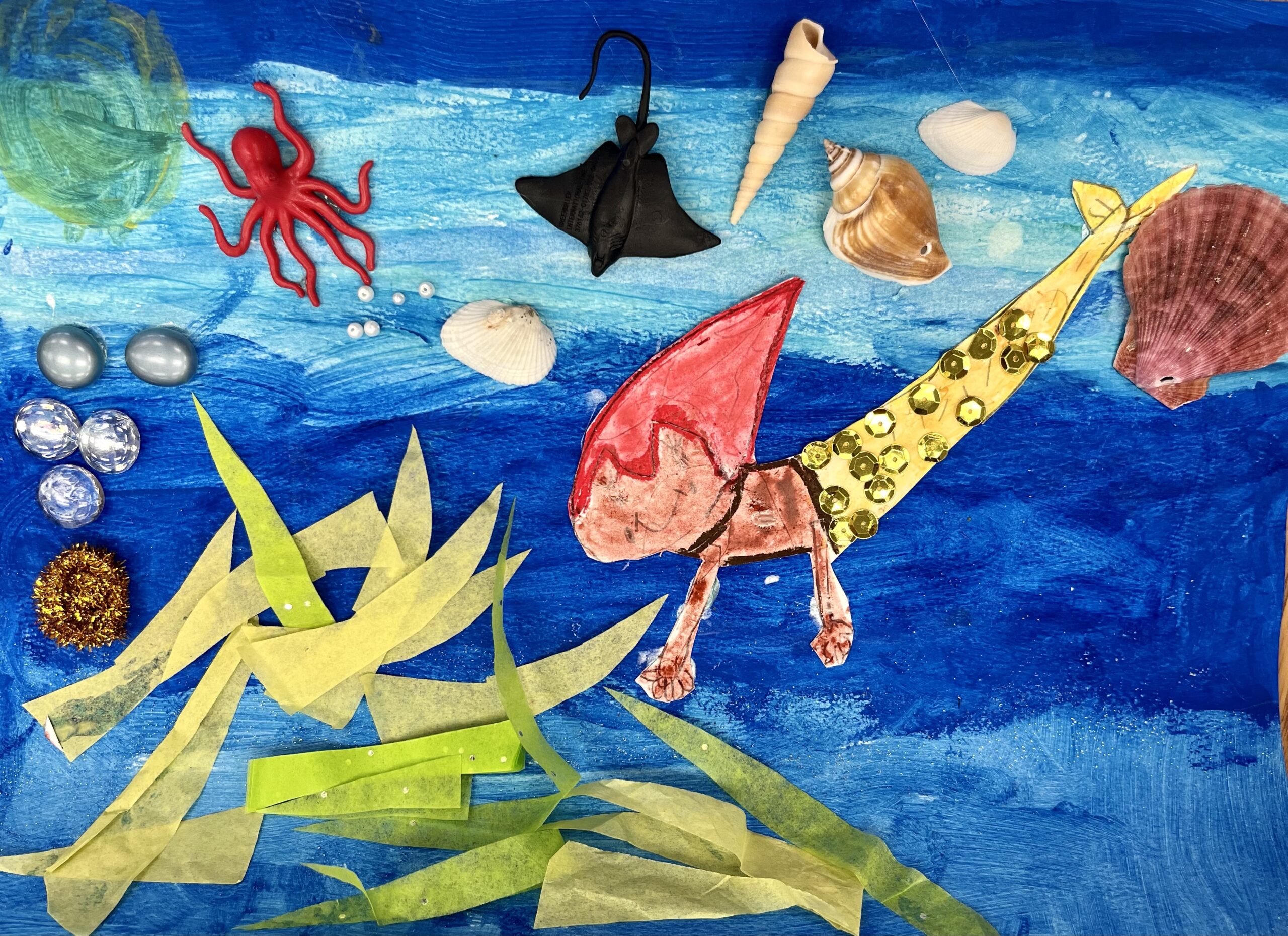 Artwork of mermaid with red hair in the ocean, surrounded by sea creatures, seaweed and seashells.