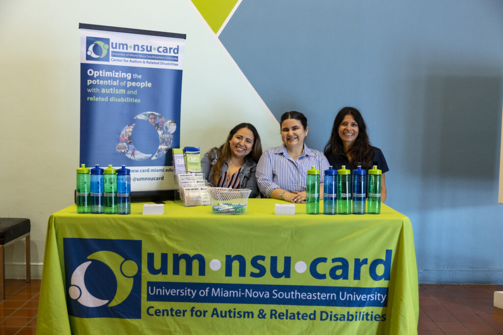 Three people sit behind a table with a green linen that reads UM-NSU CARD.