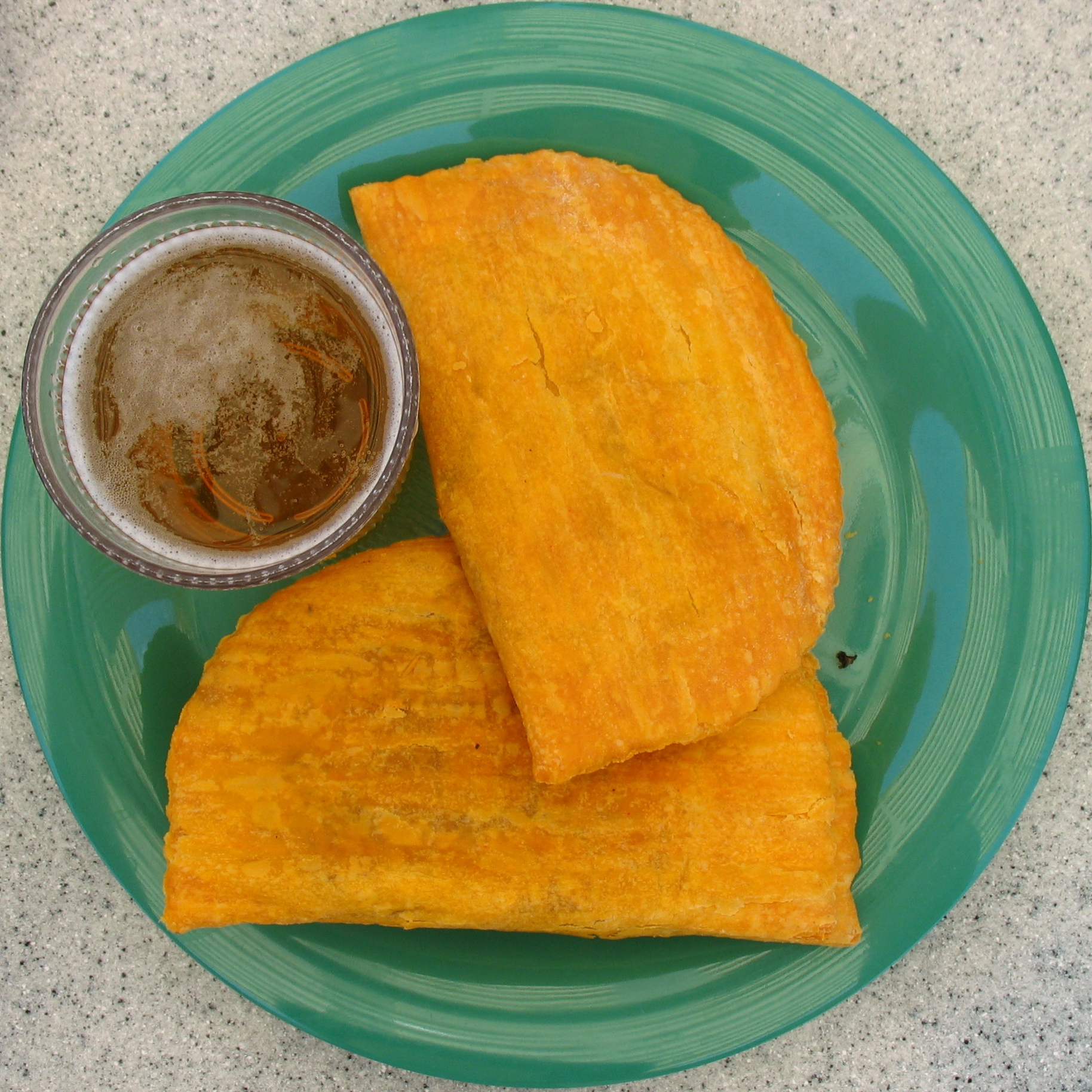 Two jamaican patties on a plate and a cup of beer