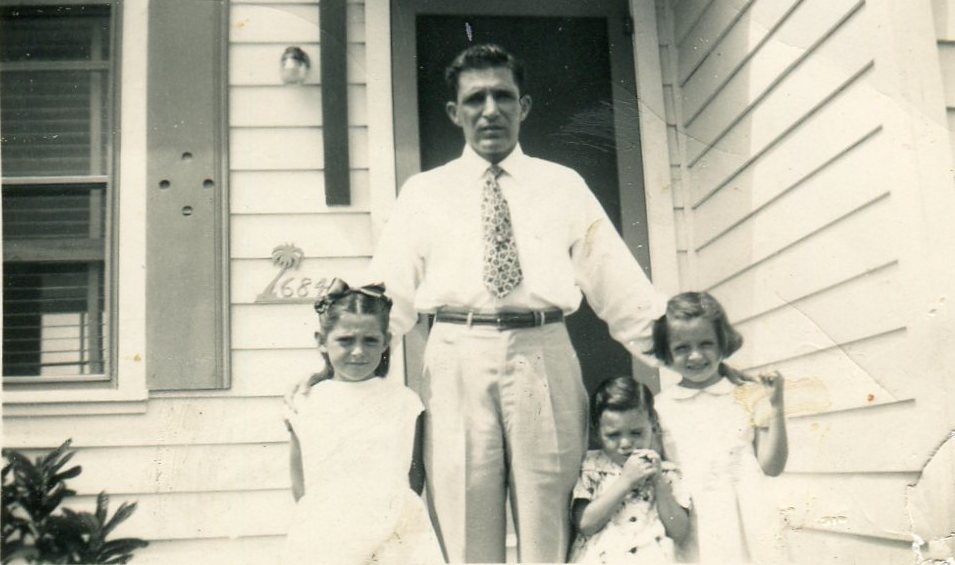 A black and white photo of a man, Aldo Garcia with his 3 children standing in front of their home.