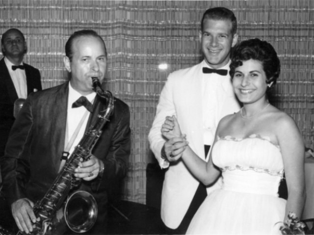 Black and white photo of a man playing the saxophone and a young couple, all in formal attire.