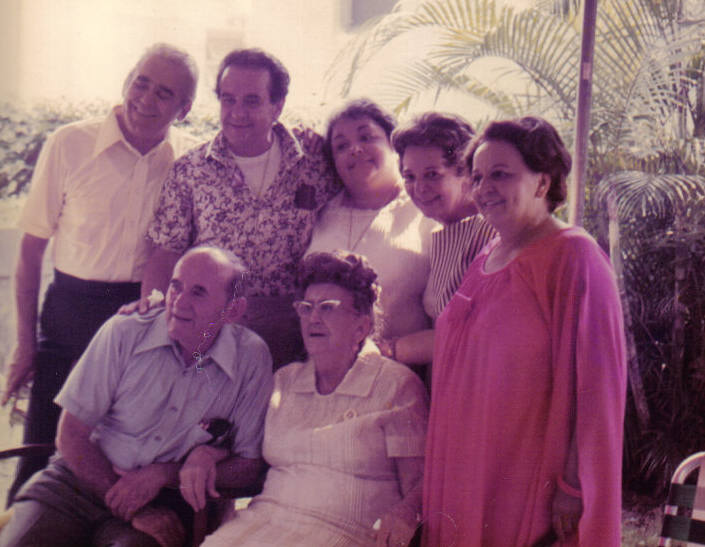 The Novoa Family including seven family members. Two older family members are seated with five family members stand behind in an embrace.