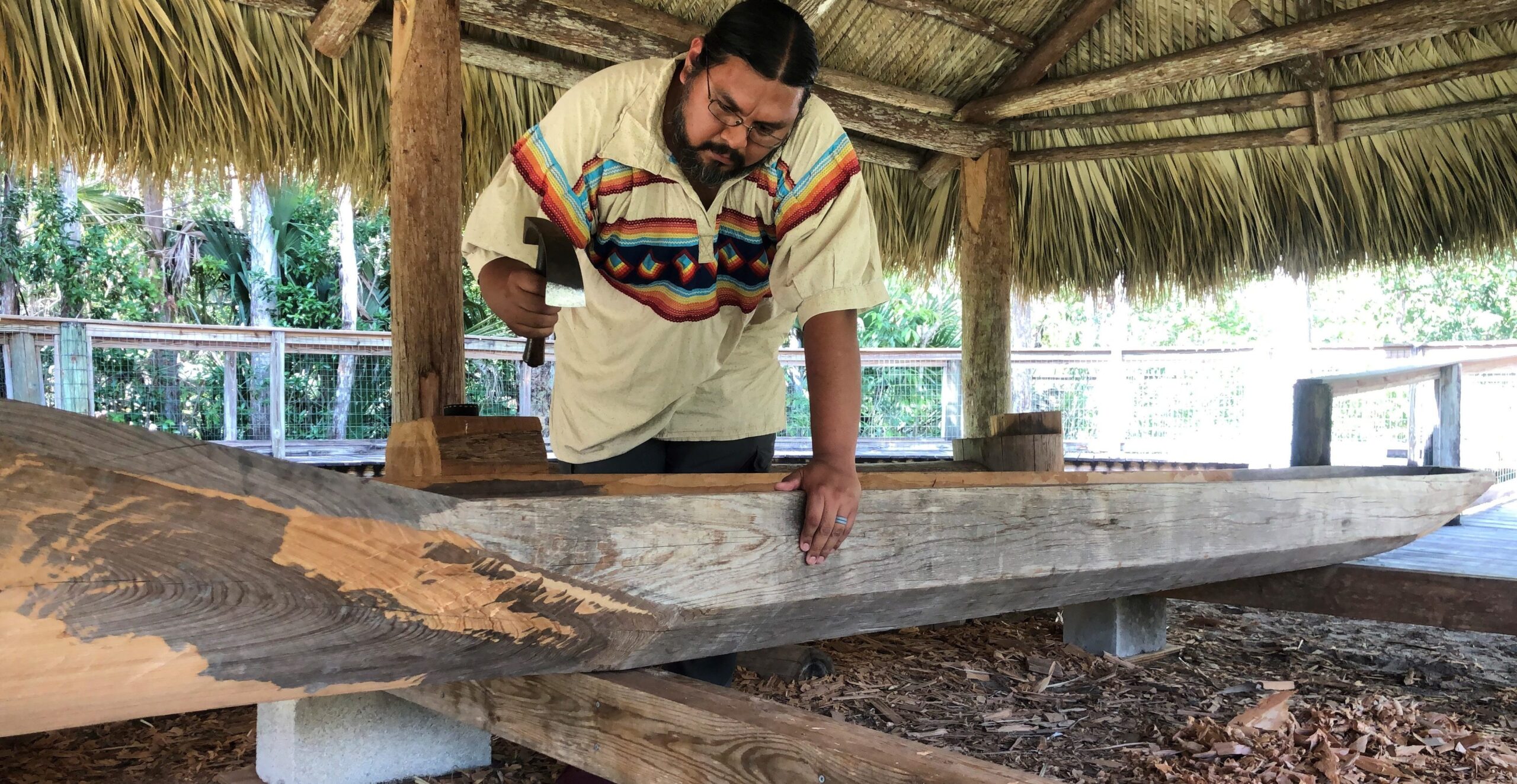 Pedro Zepeda uses a curved tool to carve out the inside of a canoe as he holds the edge with his other hand.