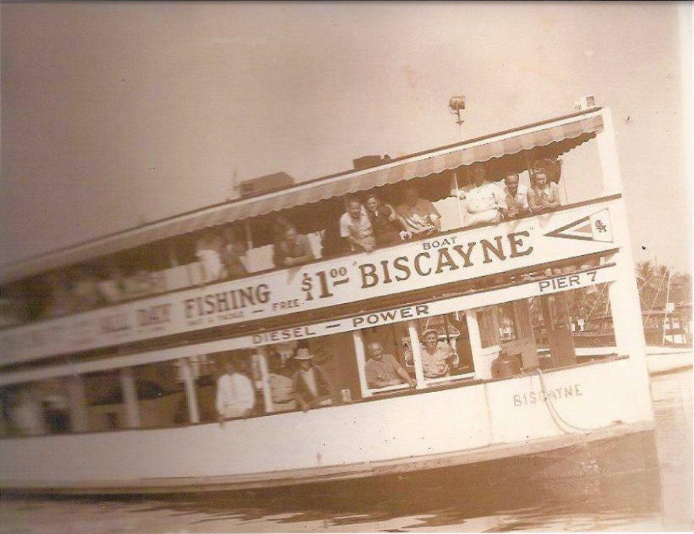 Black and white photo of a boat with many people on it. The side of the boat reads "All day fishing $1.00 Biscayne."