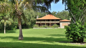 View of The Barnacle, a two-story wooden house with an orange shingled roof. A green lawn leads up to the house. Photo courtesy of the GMCVB – http://MiamiandMiamiBeach.com