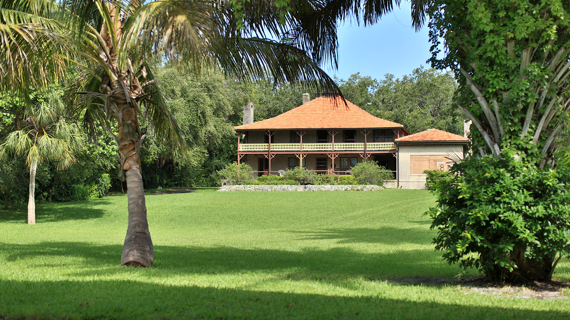 View of The Barnacle, a two-story wooden house with an orange shingled roof. A green lawn leads up to the house. Courtesy of GMCVB/miamiandbeaches.com