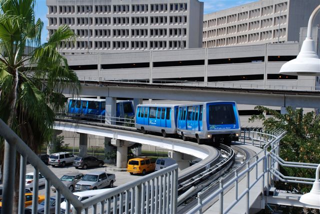 View of blue and gray Miami Metromover on elevated tracks above a parking lot.