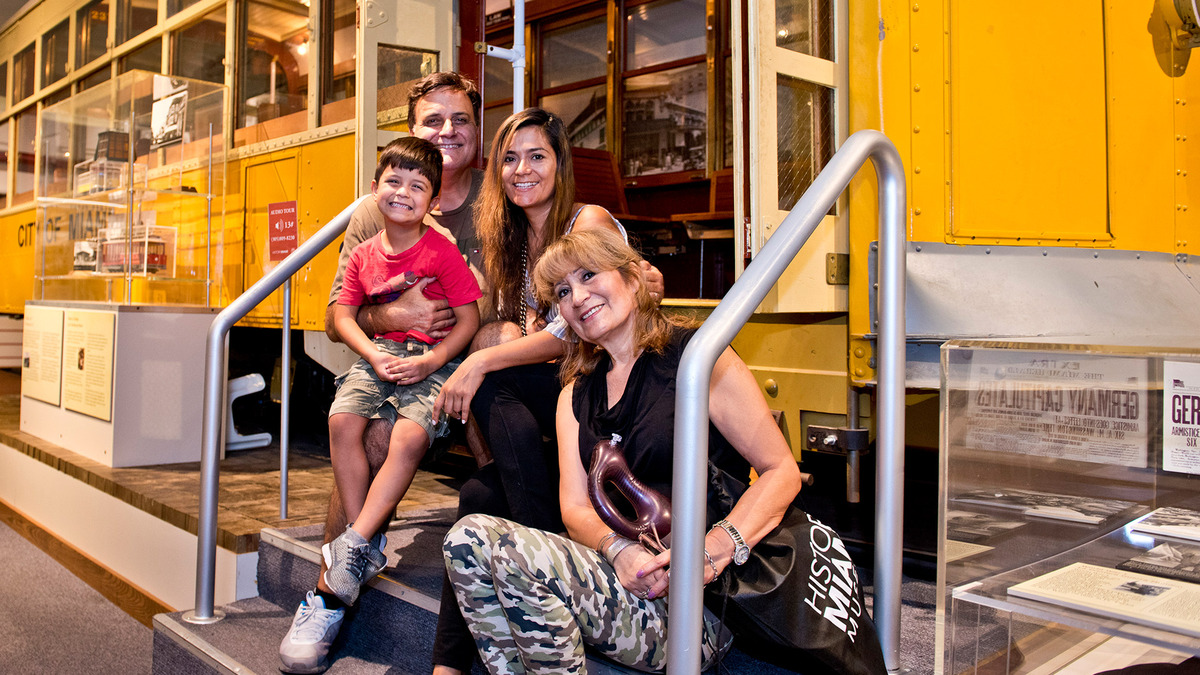 Family sitting on the steps of yellow trolley inside museum exhibition.