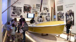 Families in the ,museum gallery looking boat.