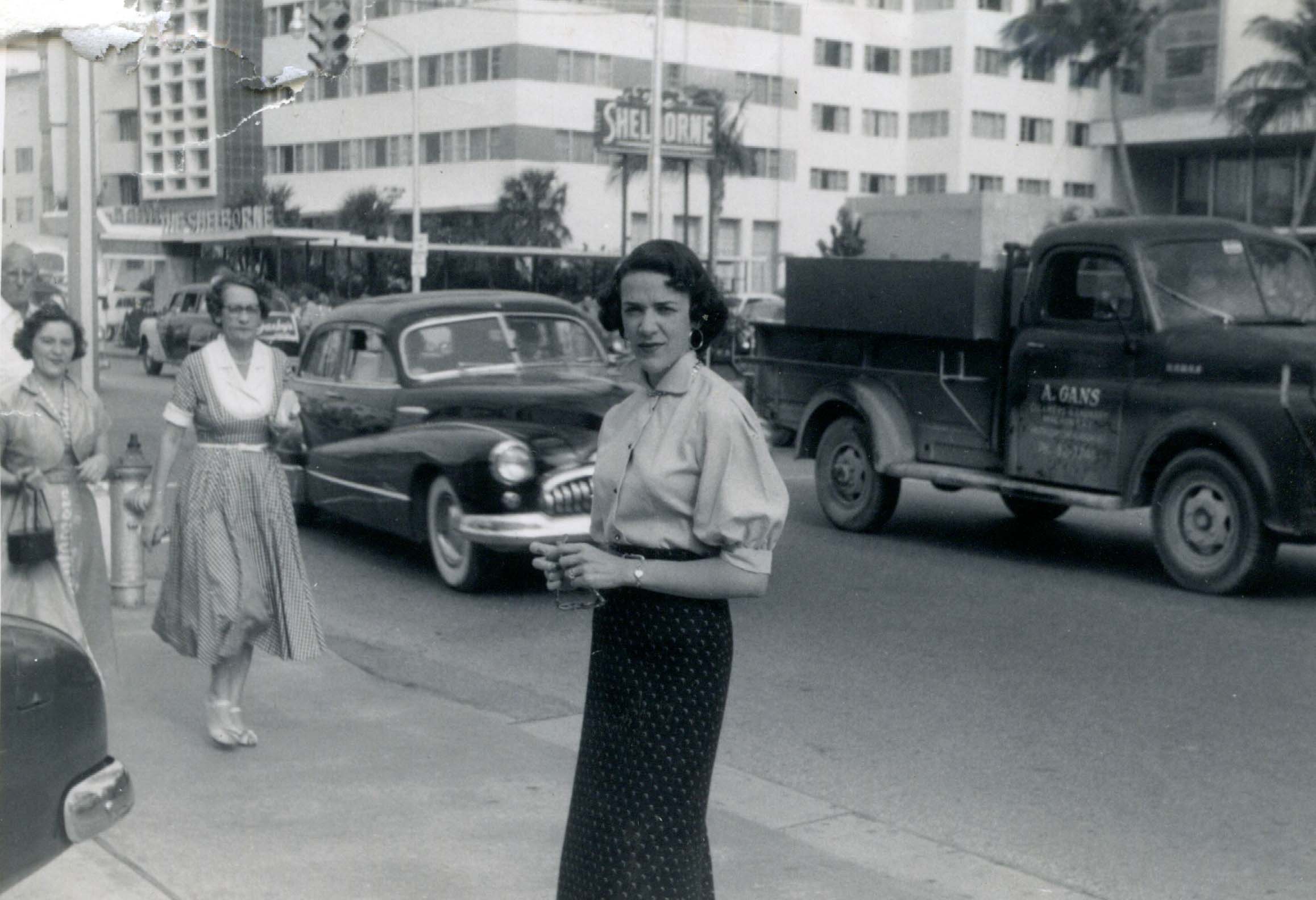 Black and white photo of a woman, Ruth Bigio, standing on Collins Avenue across from the Shelborne Hotel in 1954.
