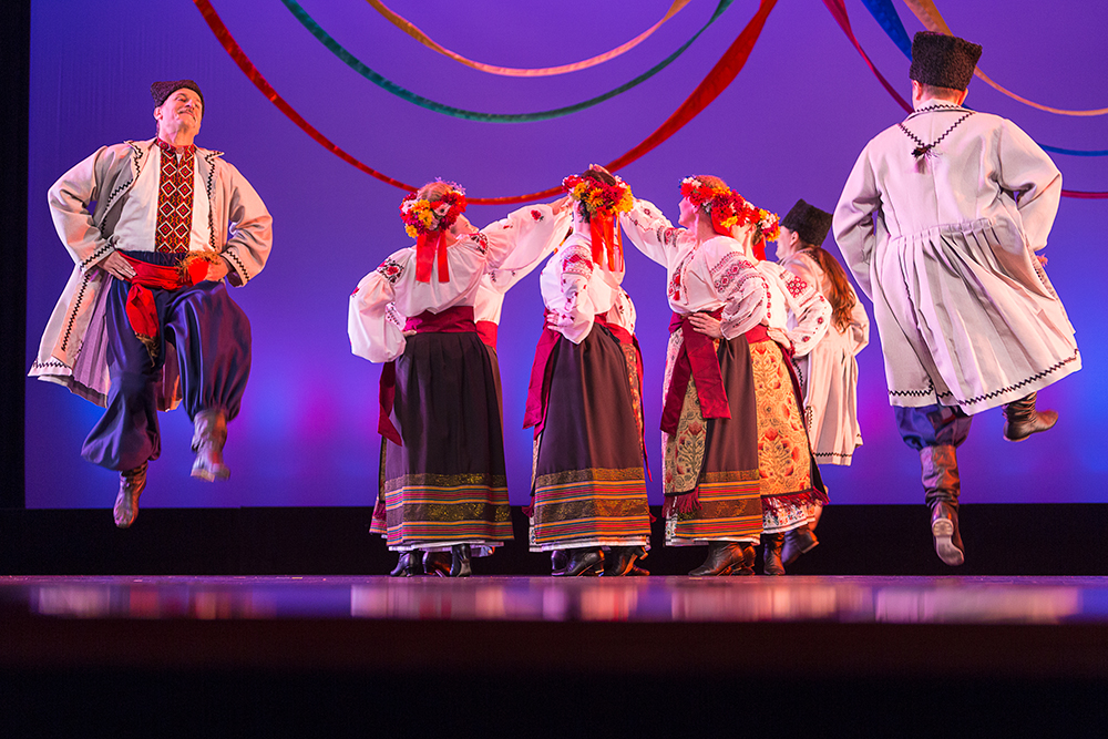 dancers perform on stage. women dance in a circle and men dance around them