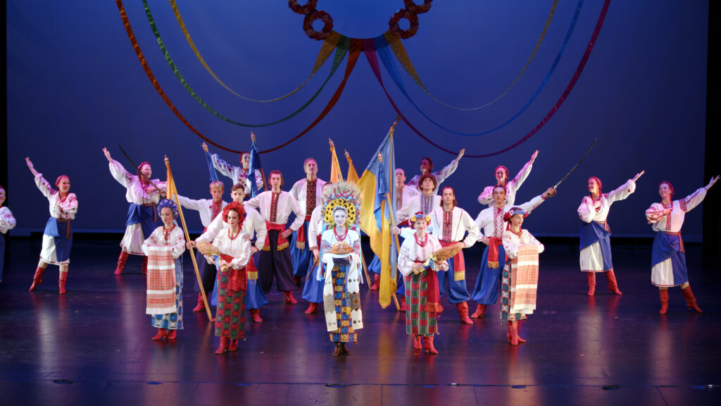 dance ensemble poses on stage with Ukrainian flag in center