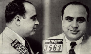 A black and white mug shot of Al Capone from the side and front.