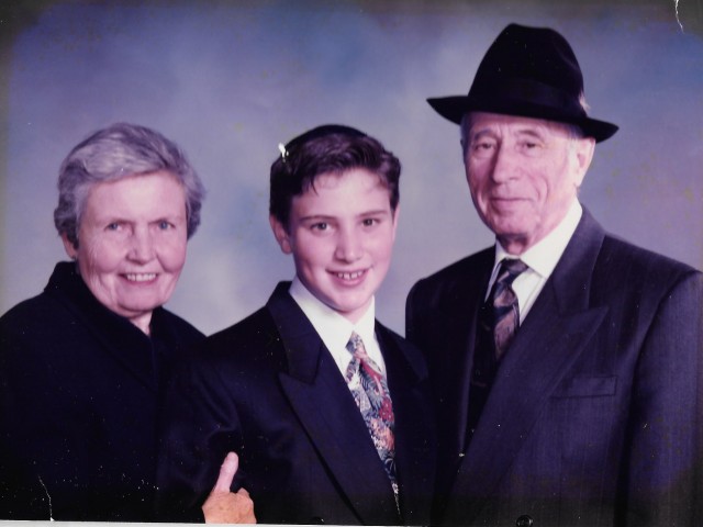 A professional photo of a young man with an older man and woman on either side. The man is wearing a hat and the woman has her hand on the young man's arm.