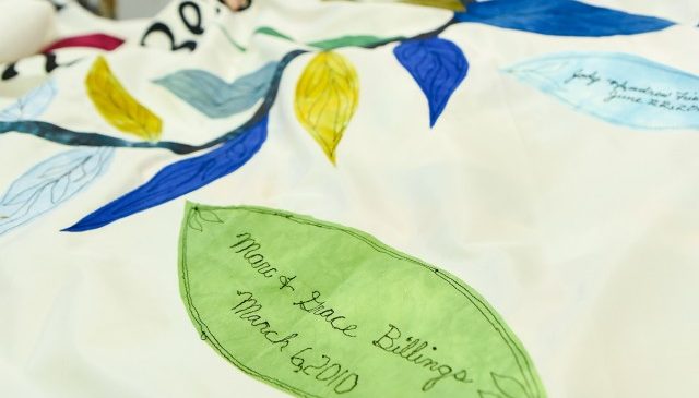 Detail of a leaf embroidered on the white backdrop of the chuppah fabric. The leaf is green and has the words 